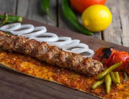 frango seeh kabab com cebola anel, Lima e tomate servido dentro prato lado Visão em de madeira mesa fundo foto