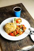 Pimenta frango arroz refeição servido dentro prato com molho, frio bebida, colher e garfo isolado em de madeira borda lado Visão do tailandês Comida foto