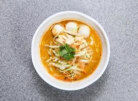 tailandês arroz macarrão dentro laksa sopa com trincado frango e peixe bola servido dentro tigela isolado em cinzento fundo topo Visão do hong kong Comida foto