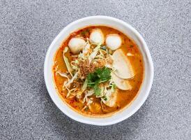 tailandês arroz macarrão dentro laksa sopa com tailandês salsichas e peixe bola servido dentro tigela isolado em cinzento fundo topo Visão do hong kong Comida foto