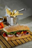 ciabatta defumado presunto sanduíche isolado em de madeira com maionese mergulho e francês fritas balde borda lado Visão do italiano velozes Comida em cinzento fundo foto