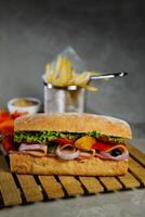 ciabatta defumado presunto sanduíche isolado em de madeira com maionese mergulho e francês fritas balde borda lado Visão do italiano velozes Comida em cinzento fundo foto