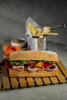 ciabatta defumado presunto sanduíche isolado em de madeira com maionese mergulho e francês fritas balde borda lado Visão do italiano velozes Comida em cinzento fundo foto