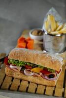 ciabatta defumado presunto sanduíche isolado em de madeira com maionese mergulho e francês fritas balde borda lado Visão do italiano velozes Comida em cinzento fundo foto