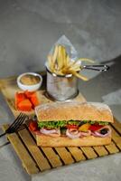 ciabatta defumado presunto sanduíche isolado em de madeira com maionese mergulho e francês fritas balde borda lado Visão do italiano velozes Comida em cinzento fundo foto