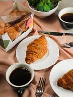 avião croissant servido em de madeira borda com copo do Preto café isolado em guardanapo com faca e garfo lado Visão do francês café da manhã cozido Comida item em cinzento fundo foto