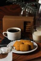 crocante biscoitos biscoitos servido dentro prato com bolacha caixa, Preto café e vidro do leite isolado em mesa lado Visão do americano cafeteria cozido Comida foto