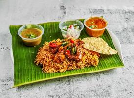 frango briyani com salada, molho picante, raita e molho servido dentro prato isolado em banana folha topo Visão do indiano e Cingapura picante Comida foto