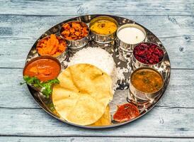 sul indiano frango refeição thali tikka Masala, Curry, arroz, raita, Korma, Kesari Halwa e chapati servido dentro prato isolado em de madeira mesa topo Visão do indiano picante Comida foto