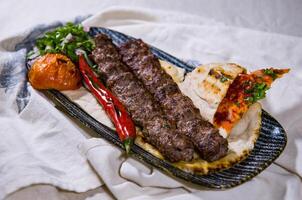 carne bovina, Cordeiro ou Carneiro seeh kabab carne Kebab com Pão Pita pão, tomate e cebola servido dentro prato isolado em Comida mesa topo Visão do meio leste especiarias foto