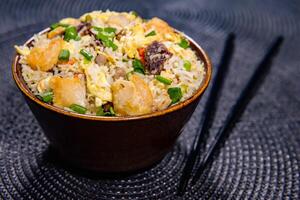 misturado frito arroz com com frango, cenoura, Primavera cebola, ovo e pauzinhos servido dentro tigela lado Visão do chinês Comida foto