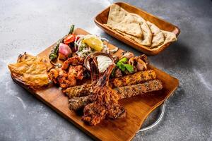 misturar grade com shish tawook, Carneiro cortar, campeão, frango kabab, carne Churrasquinho, tikka boti, reshmi e malai Pão Pita pão, nan, tandoori roti, raita, mergulhar, salada e limão servido dentro de madeira borda topo Visão foto