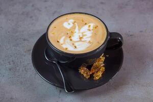 quente salgado caramelo café com leite arte servindo dentro café copo com colher e feijões lado Visão em cinzento fundo foto