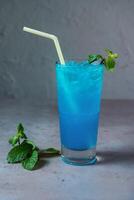saudável azul lagoa Mojito refrigerante servido dentro vidro com Palha lado Visão em cinzento fundo foto