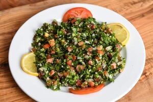 tabule salada com tomate, pepino, verde coentro, cebola e limão servido dentro prato isolado em de madeira mesa topo Visão meio Oriental aperitivos Comida foto