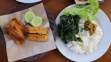 ayam Goreng lalapan. consistindo do arroz, frito frango, tofu, tempeh, vegetais, e samba foto