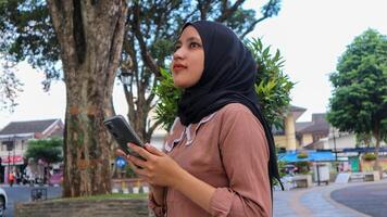 retrato do muçulmano mulher usando Móvel telefone lendo mensagem às cidade parque. desfrutando, relaxante final de semana foto