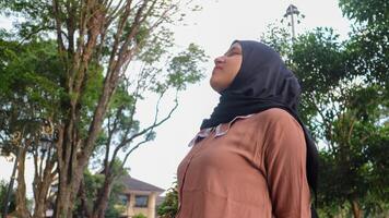 lindo muçulmano mulher dentro hijab relaxante respiração fresco ar em pé dentro uma parque. foto