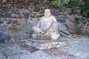 Cherkasy, Ucrânia - Outubro 20, 2021 alegre buddah concreto cinzento estátua fechar para branco lótus budista têmpora foto