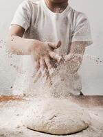 colheita irreconhecível criança pessoa palmas mãos com farinha enquanto cozinhando pão aspersão branco farinha sobre blob do massa. vertical. cópia de espaço inferior foto