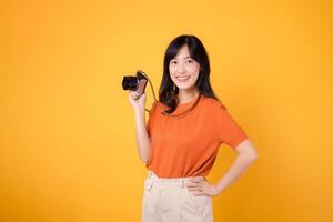 jovem ásia mulher com uma Câmera isolado em amarelo fundo, pronto para uma Diversão aventura percorrer. positivo feriado vibrações conceito. foto