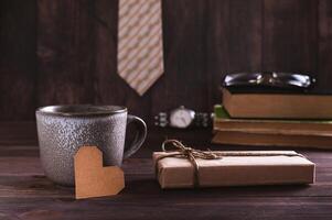 do pai dia conceito cartão coração perto uma caneca, presente, gravata, livros e óculos em a mesa foto