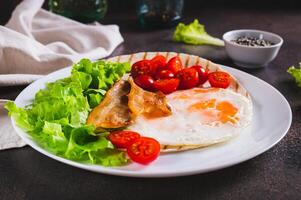 apetitoso tacos com frito ovo, bacon, tomate e alface em uma prato em a mesa foto
