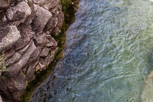 rio fluindo ao longo uma rochoso penhasco Próximo para uma cachoeira, com musgo e reflexões dentro a água. Visão a partir de acima. fundo. textura. horizontal. foto