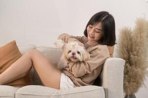 feliz jovem ásia mulher abraço e gastos Tempo com fofa cachorro dentro vivo sala. foto