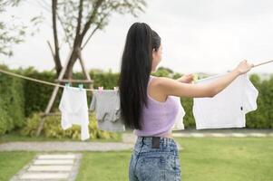 jovem ásia mulher suspensão lavanderia em lavando linha para secagem contra azul céu ao ar livre foto