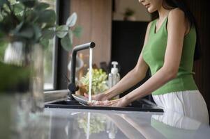 ásia mulher lavando pratos dentro a cozinha Pia às casa foto