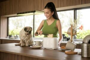 ásia mulher preparando café e torrada pão para café da manhã apreciar com cachorro às a cozinha mesa dentro a manhã foto