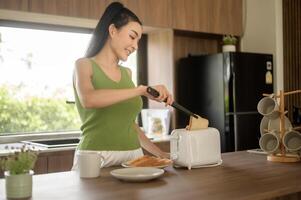 ásia mulher preparando café e torrada pão para café da manhã às a cozinha mesa dentro a manhã foto
