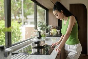 ásia mulher cozinhando e cheirando degustação sopa dentro uma Panela dentro a cozinha mesa às lar. foto