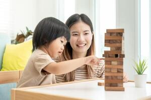 Ásia feliz solteiro mãe jogando Aprendendo jogos janga com a pequeno garoto. engraçado família é feliz e animado dentro a casa. pai e filho tendo Diversão gastos Tempo junto. feriado, fim de semana, vago. foto