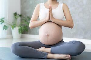 grávida mulher fazendo ioga em exercício esteira. meditando para curto prazo parto do meditando atraente grávida fêmea lazer e relaxar, respiração e calma com ioga. auto Cuidado foto