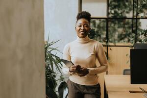 jovem africano americano mulher em pé com digital tábua às a escritório foto