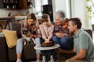 feliz família a comemorar avós aniversário com bolo dentro uma acolhedor vivo quarto foto