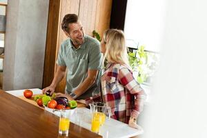 sorridente homem e mulher cortar fresco legumes em uma cozinha ilha, desfrutando uma saudável cozinhando atividade juntos foto