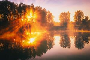 alvorecer em uma lago ou rio com uma céu refletido dentro a água, bétula árvores em a costa e a raios solares quebra através eles e névoa dentro outono. estética do vintage filme. foto