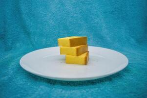 três peças do queijo bolo em uma branco prato com uma turquesa pano fundo foto
