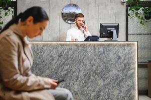 retrato do uma jovem masculino recepcionista dentro uma hotel lobby vestindo uma branco camisa foto