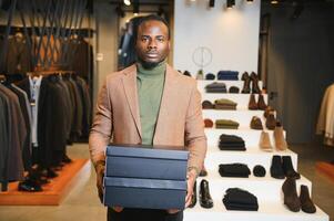 alegre africano americano homem carregando compras bolsas dentro roupas loja. moda boutique foto