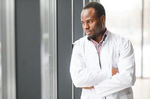 africano médico dentro corredor . retrato do confiante masculino médico usando tábua computador dentro clínica com cópia de espaço foto