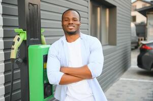 retrato do uma jovem homem em pé com cobrando cabo perto a cobrando estação. conceito do velozes casa carro carregadores. foto