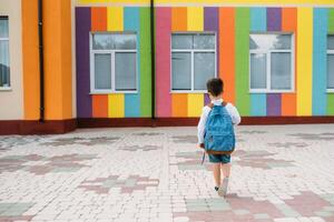 pequeno Garoto indo costas para escola. criança com mochila e livros em primeiro escola dia. costas visualizar. escola conceito. costas para escola. foto