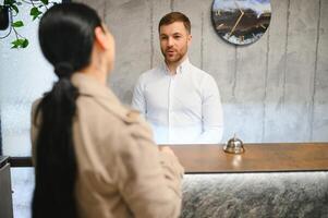 retrato do uma jovem masculino recepcionista dentro uma hotel lobby vestindo uma branco camisa foto