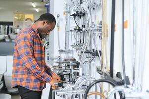 uma ampla seleção do água torneiras. africano americano homem escolhe uma produtos dentro uma sanitário porcelana loja foto