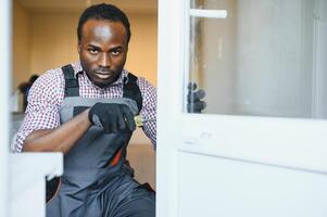 jovem africano faz-tudo dentro uniforme fixação vidro janela com Chave de fenda foto