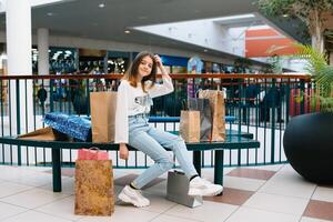 lindo jovem mãe e Adolescência filha estão segurando compras bolsas, compras dentro shopping center. família compras foto